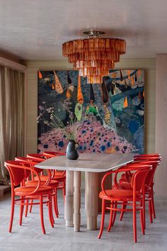 a dining room table with red chairs and a large painting on the wall behind it