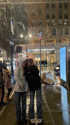 two people are standing in the rain on a city street with their arms around each other