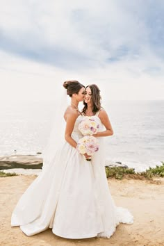 two brides kissing on the beach in front of the ocean