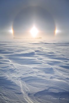 two rainbows are seen in the distance over snow covered ground with bright light coming from behind them