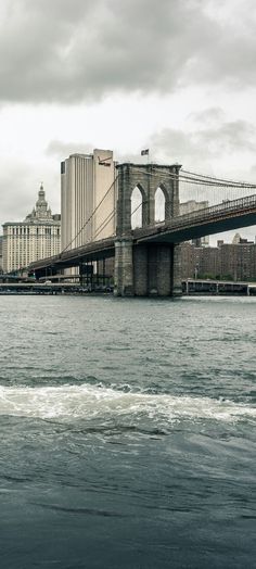 a boat is going under the brooklyn bridge in new york city, on a cloudy day