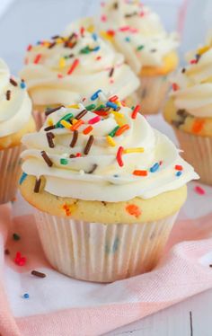 cupcakes with white frosting and sprinkles on a pink napkin