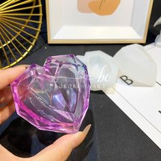 a hand holding a pink heart shaped object in front of a table with other items