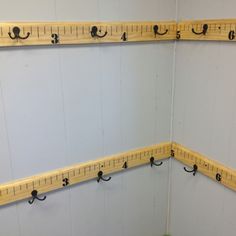 two wooden rulers are hanging on the wall with hooks in front of them and one has a measuring tape attached to it