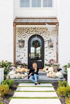 a woman sitting on steps in front of a house decorated with pumpkins and bats