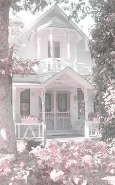 a white house with pink flowers in front of it and trees around the porch area