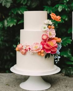 a white wedding cake with flowers on top and greenery in the backround