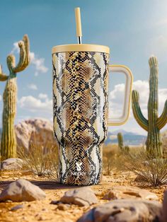 a cup with a straw in it sitting on the ground next to some cacti