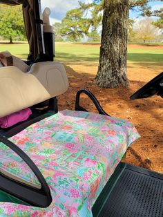 the back seat of a golf cart is covered with a colorful floral print fabric and sits next to a tree