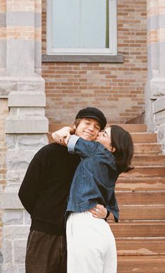 two people standing next to each other in front of a building with stairs and windows