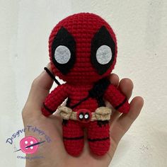 a hand holding a small crocheted deadpool doll