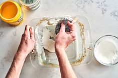 two hands are decorating a cake with icing and sprinkles on a marble table