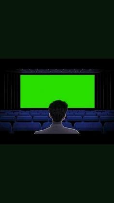 a man sitting in front of a green screen at a movie theater with his head turned to the side