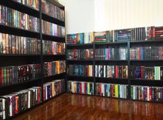 a room filled with lots of dvd's on black shelving units next to a wooden floor