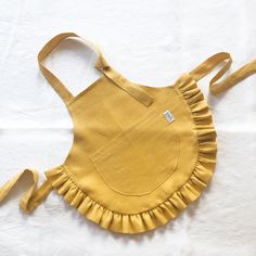 a yellow apron with ruffles on it sitting on top of a white sheet