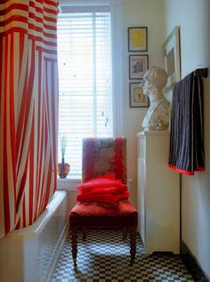 a red chair sitting in front of a window next to a checkerboard floor