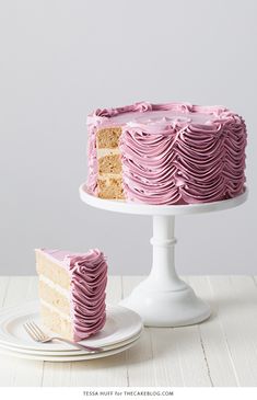 a cake with pink frosting on a white plate next to a piece of cake