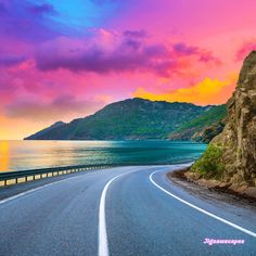 an empty road next to the ocean at sunset