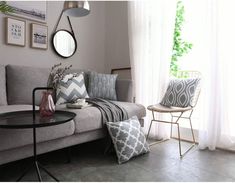 a living room with a gray couch and white curtains on the window sill next to a round coffee table