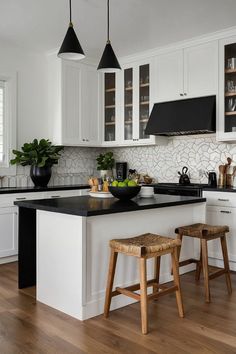 a kitchen with white cabinets, black counter tops and two stools in front of the island