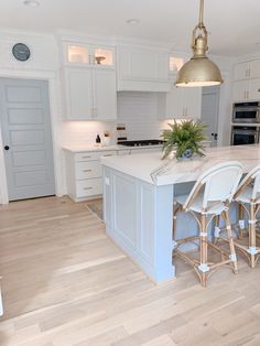 a large kitchen with white cabinets and an island in the middle is surrounded by bar stools