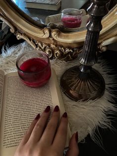 a woman is reading a book and holding a glass of red liquid in front of her