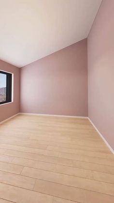 an empty room with pink walls and wooden floors, looking out the window at mountains