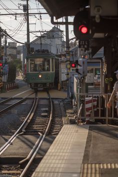 a green train traveling down tracks next to a loading platform with people standing on it