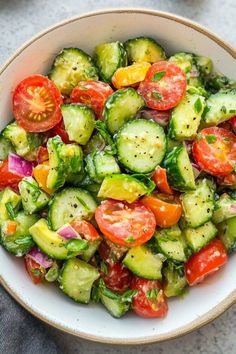 a white bowl filled with cucumber and tomato salad on top of a table