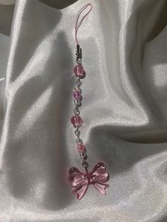 a necklace with pink beads and a bow on it's end is laying on a white fabric