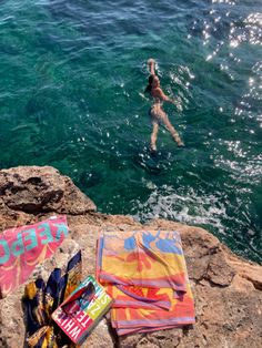 a woman swimming in the ocean next to some towels and other items on the rocks