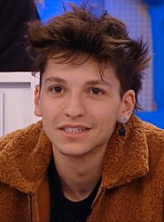 the young man is smiling and wearing earrings in front of an interview set