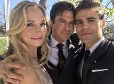 two men and a woman are posing for a picture in front of a tree with their arms around each other