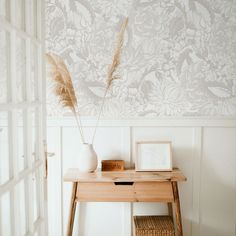 a wooden table with a vase on top of it next to a wallpapered wall