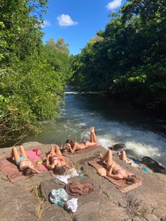 three people laying on rocks in front of a river with trees and water behind them