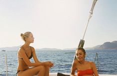 two women in bikinis sitting on the deck of a boat looking at each other