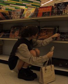 a woman sitting on the ground in front of a book shelf holding onto a purse