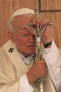 an older man holding up a crucifix in front of his face