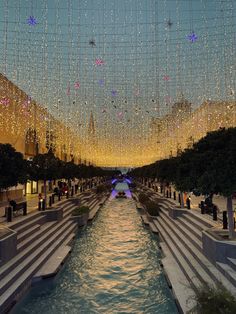 the lights are hanging from the ceiling over the water in this city square area, and it looks like they have been lit up at night