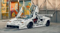 a white sports car parked in front of a building with its doors open and it's door opened