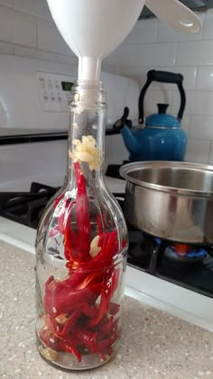 a glass bottle filled with red peppers sitting on top of a counter next to a stove