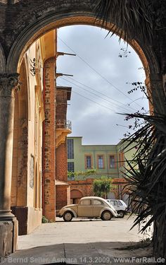 an old car is parked in front of a brick building with arches on the side