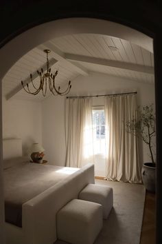 a bed room with a neatly made bed and a chandelier hanging from the ceiling