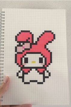 a hand holding a notebook with an image of hello kitty in the form of a pixel