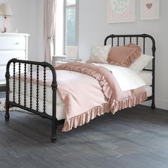 a bed with pink sheets and pillows in a bedroom next to a window, on top of a wooden floor