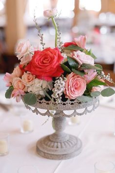 a vase filled with pink and red flowers on top of a white table cloth covered table