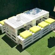 an outdoor table and bench made out of pallet wood with yellow cushions on the grass