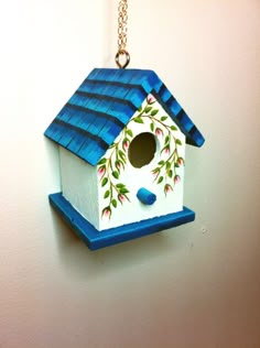 a birdhouse hanging from a chain on the wall with blue roof and flowers painted on it