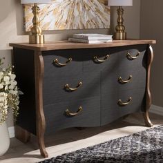 a black and gold dresser with two lamps on it's sides, in front of a painting