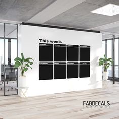 this week wall decal is in an office with wooden floors and large windows, along with potted plants